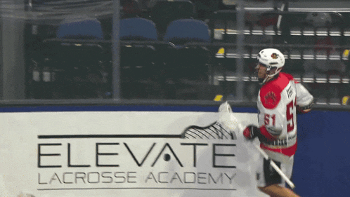 a lacrosse player in front of a elevate lacrosse academy sign