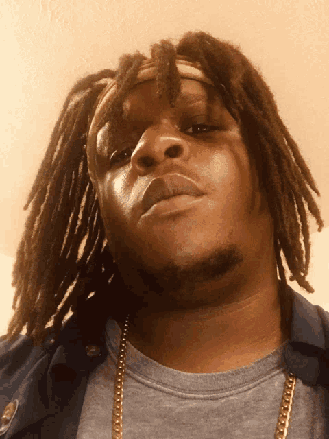 a man with dreadlocks is wearing a grey shirt and a gold chain