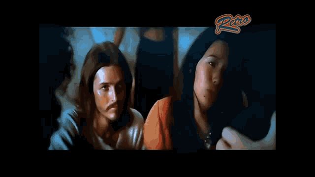 a man with long hair and a mustache is standing next to a woman with long hair in a dark room .
