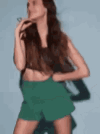 a woman in a crop top and green shorts is standing in front of a blue wall .
