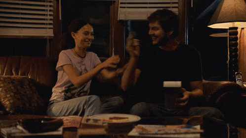 a man and a woman are sitting on a couch laughing and playing with each other