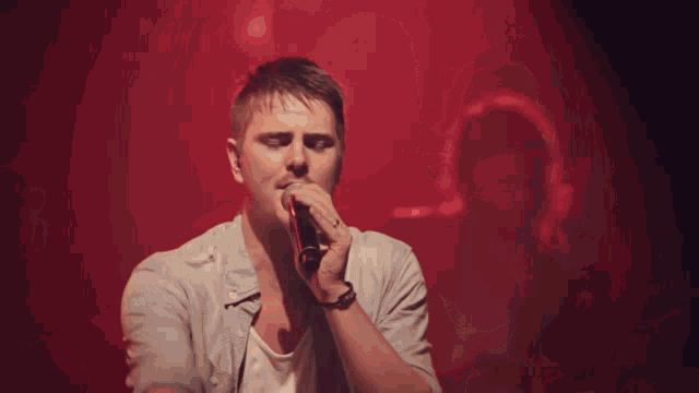 a man sings into a microphone with a red background