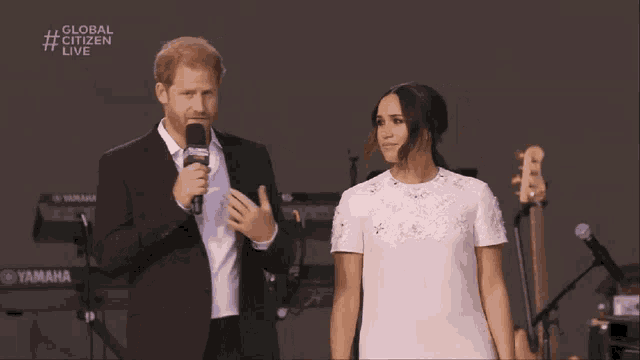 a man in a suit and a woman in a white dress are standing next to each other in front of a global citizen live sign