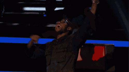 a man wearing glasses is sitting in a red chair with his arms in the air