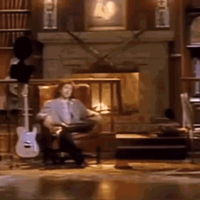a man is sitting in a chair reading a book in a living room with a guitar .