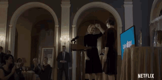 two women are dancing in front of a group of women and the word netflix is on the bottom of the screen .