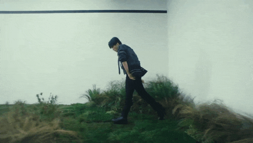 a man in a black jacket is walking through a grassy area