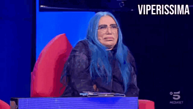 a woman with blue hair is sitting in front of a tv screen that says viperissima on it