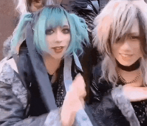 a couple of girls with blue hair are standing next to each other and smiling .