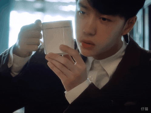 a man in a suit is drinking from a cup with chinese writing on the bottom