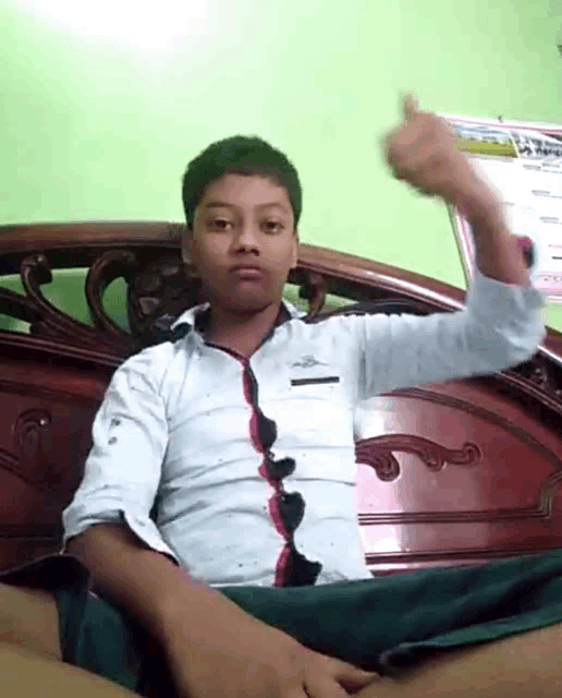 a young boy is giving a thumbs up sign while sitting on a bed