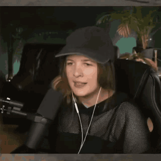 a woman wearing a hat and headphones is sitting in a chair in front of a microphone