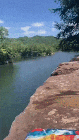a rainbow colored towel sits on a rock overlooking a lake