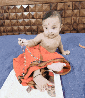 a baby is sitting on a bed and holding a string of beads