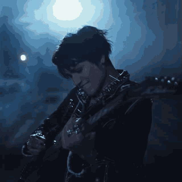 a man in a black jacket is playing a guitar in a dark room