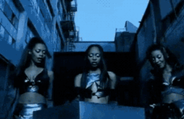 three women are standing in a dark alleyway in front of a building