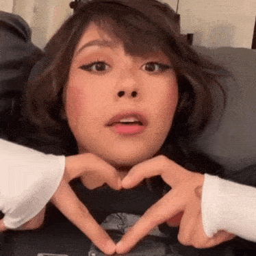 a woman is making a heart shape with her hands while sitting on a couch .