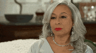 a woman with gray hair and red lipstick is wearing a silver necklace and earrings