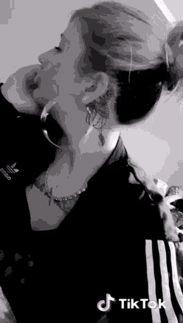 a black and white photo of a woman with a tattoo on her neck and earrings .