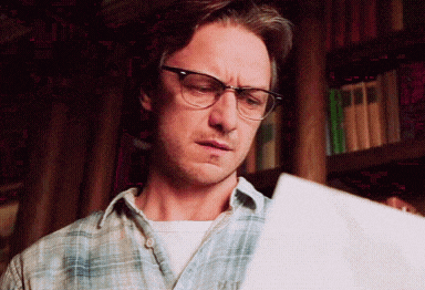 a man wearing glasses and a plaid shirt is reading a piece of paper