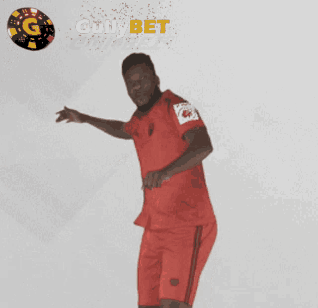 a man in a red shirt stands with his arms outstretched in front of a gullybet logo