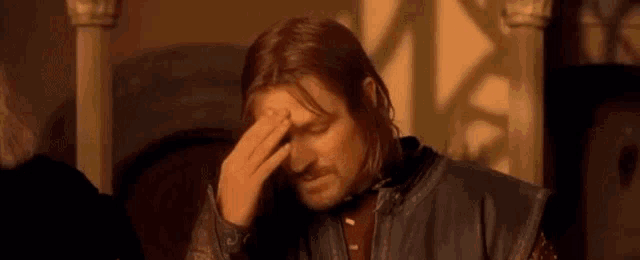 a man with long hair and a beard is holding his head in pain .