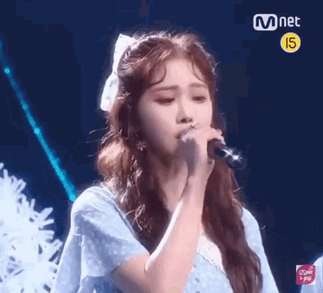 a girl in a blue dress is singing into a microphone on a stage .