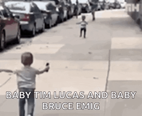 a little boy is riding a bike down a street while another little boy looks on .