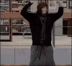 a woman in a black sweater and grey skirt is dancing in a store