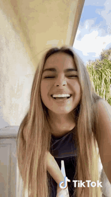 a woman with long blonde hair is laughing with her eyes closed and her tongue out .