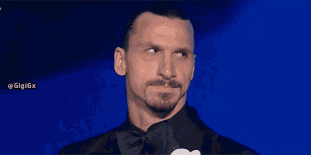 a man with a beard wearing a tuxedo and bow tie looks to the side