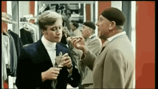 a man in a suit is talking to another man in a hat in a clothing store .