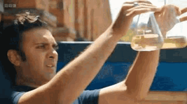 a man is holding a beaker over his head and looking at it .
