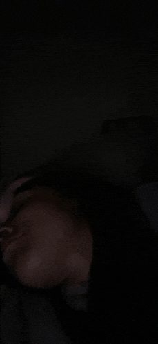 a person is laying on a bed in the dark with their eyes closed .