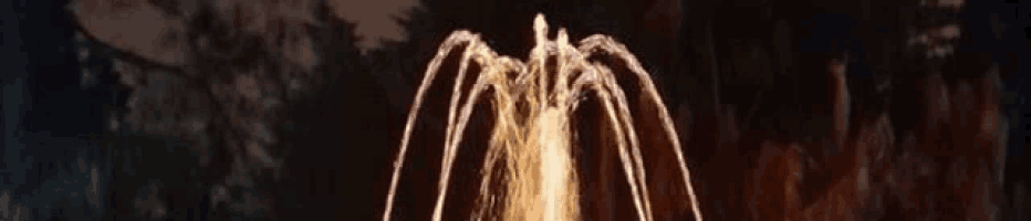 a close up of a fountain at night with a dark background