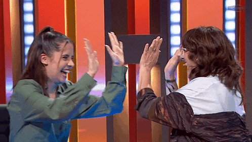 two women are giving each other a high five in front of a red wall