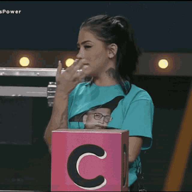 a woman covering her mouth while standing next to a box with the letter c on it