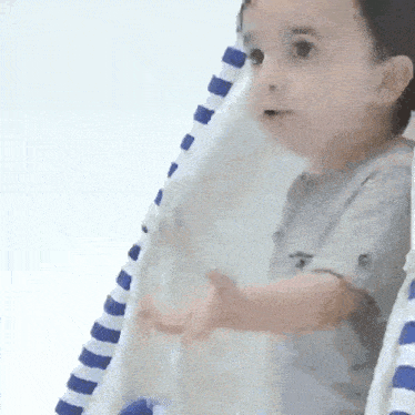a baby is standing in front of a blue and white striped towel .