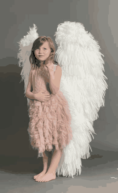 a little girl wearing a pink dress and white feathered angel wings