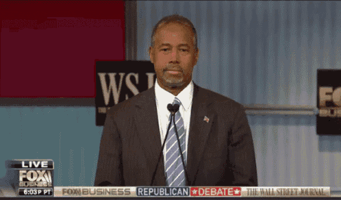 a man in a suit and tie stands in front of a microphone in front of a wall street journal banner