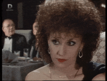 a woman sitting at a table with a man in a tuxedo behind her and a sign that says drama on it