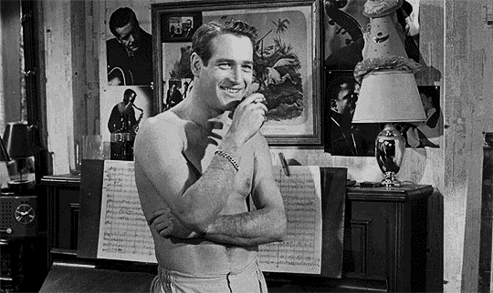 a shirtless man is standing in a room with his arms crossed and a lamp .