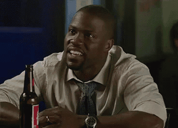 a man in a suit and tie is sitting at a table with a bottle of beer in front of him .