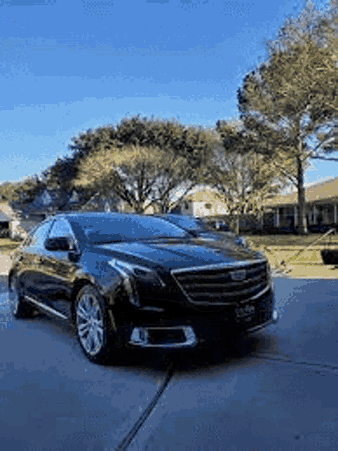 a black car is parked in a driveway in front of a house with trees in the background .