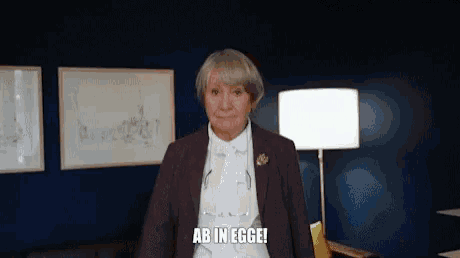 an older woman in a suit and tie is standing in a living room and says `` ab in egge '' .