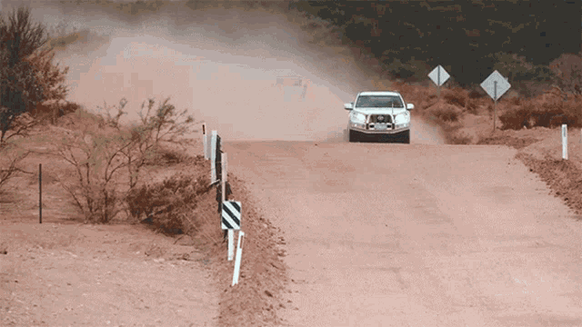 a white car is driving down a dirt road with a sign that says ' a ' on it