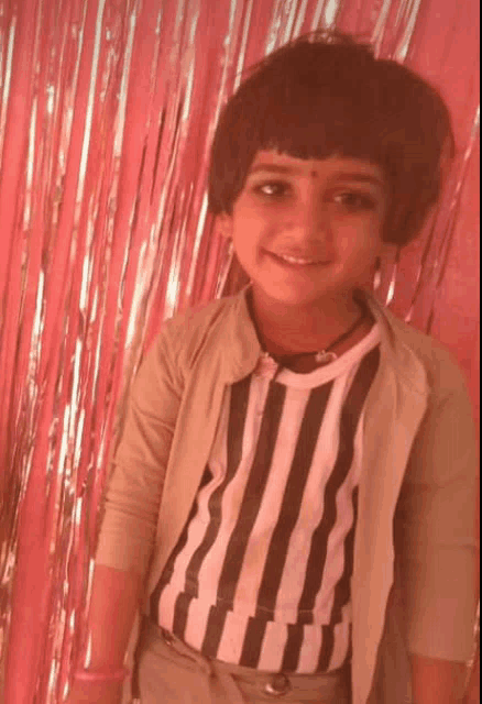 a young girl wearing a striped shirt is smiling in front of a pink background
