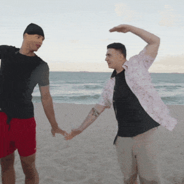 a man with a tattoo on his arm holds hands with another man on a beach