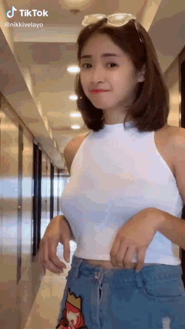 a woman in a white tank top and blue shorts is standing in a hallway .