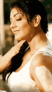a woman in a white tank top is smiling with her eyes closed and a red car in the background